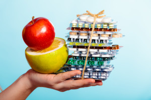 Human hand holding stack of pills and fruits on blue.